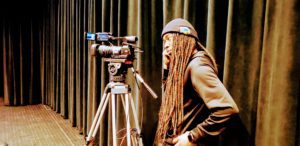 A man with dreadlocks standing in front of a camera.